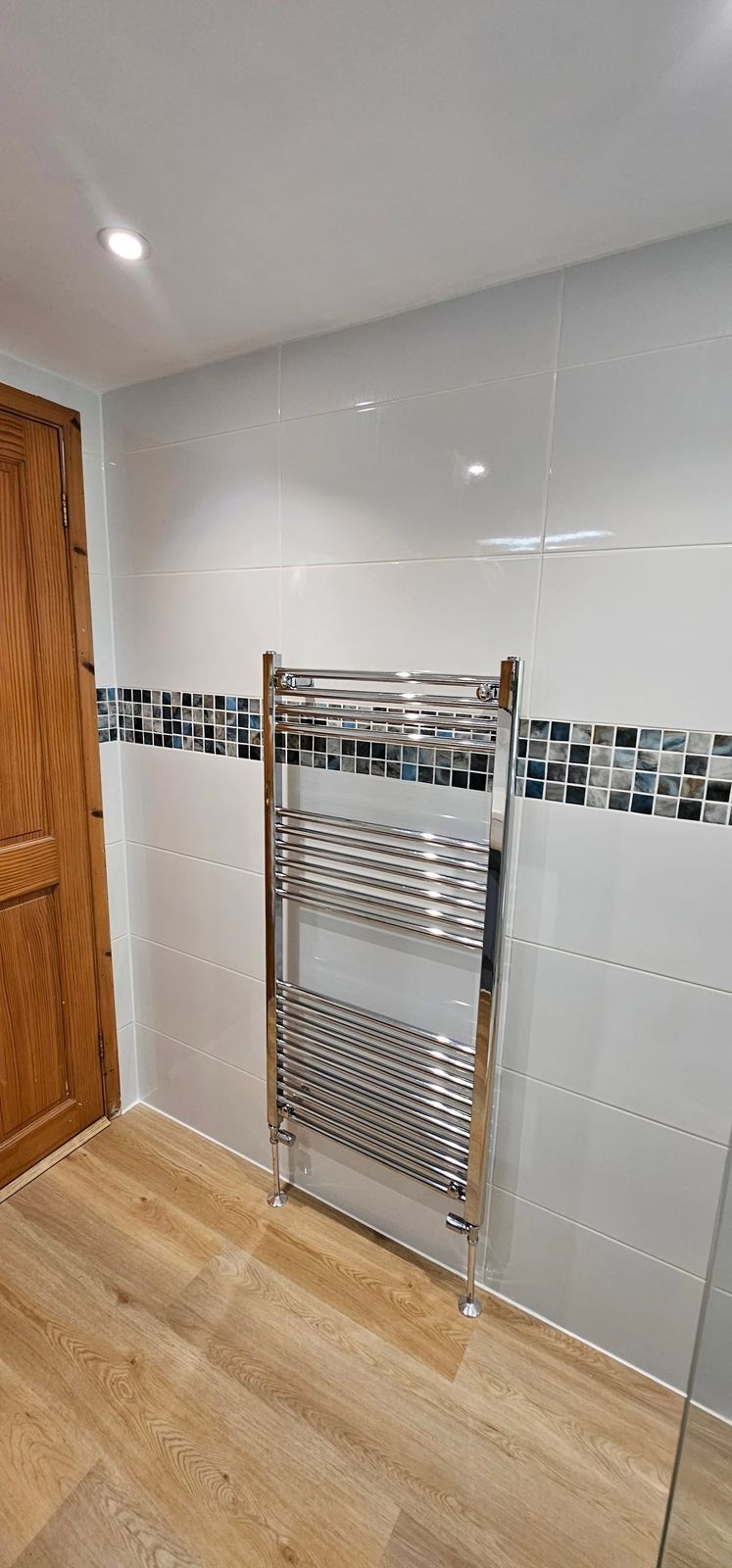 Chrome towel radiator on white tiles with a mosaic border