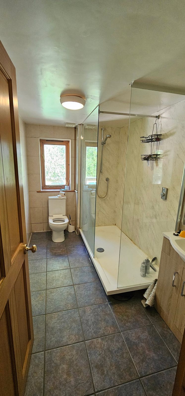 The bathroom before the refit, with an old shower tray, tiled walls and a dark tiled floor