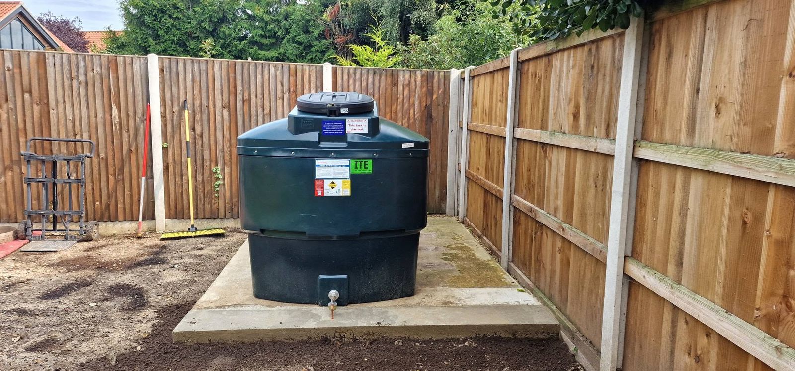 Green oil tank on a concrete base beside a fence