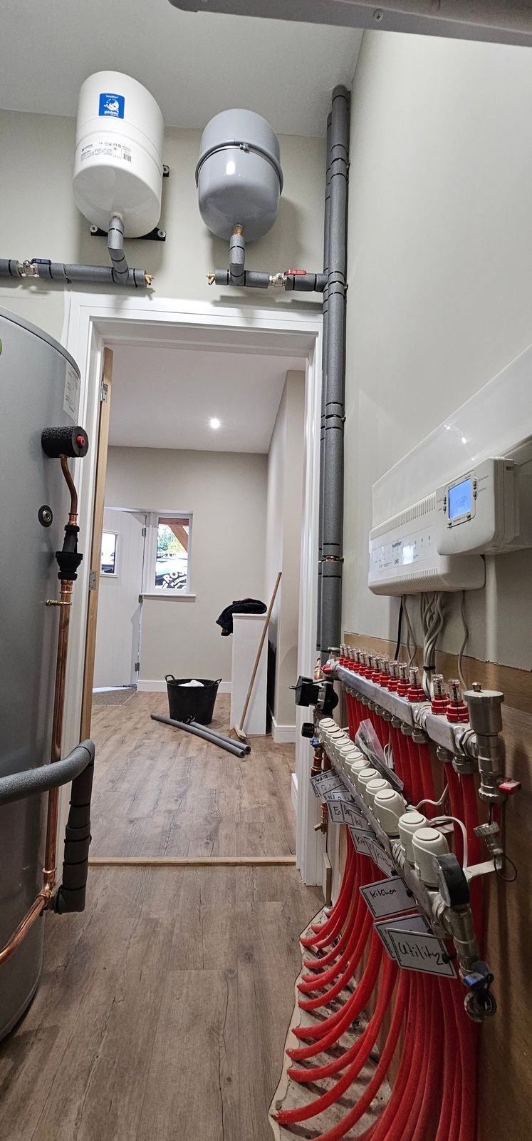 Underfloor heating manifold with red pipes, expansion vessels and a cylinder