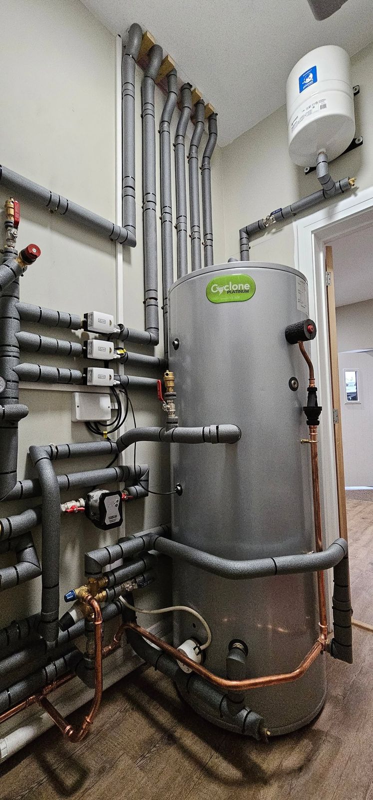Unvented hot water cylinder with grey lagged pipework in a plant room