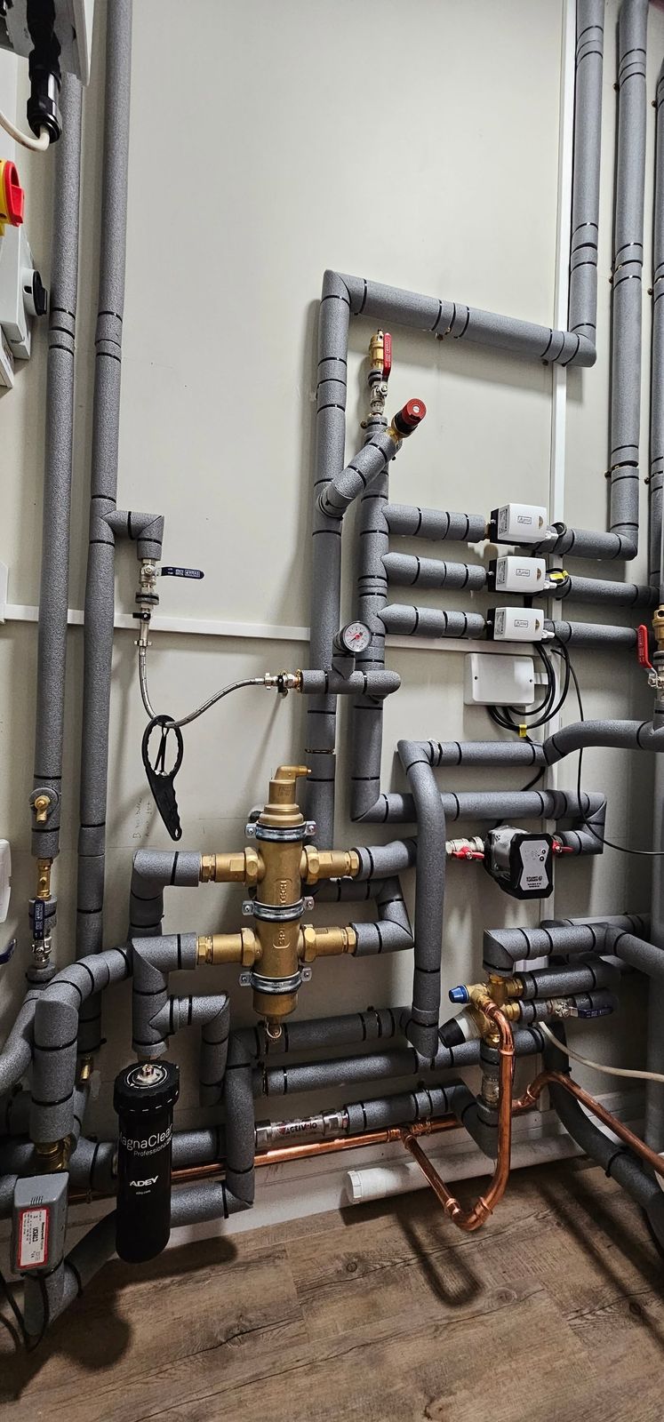 Valves, pumps and lagged pipework on a plant room wall