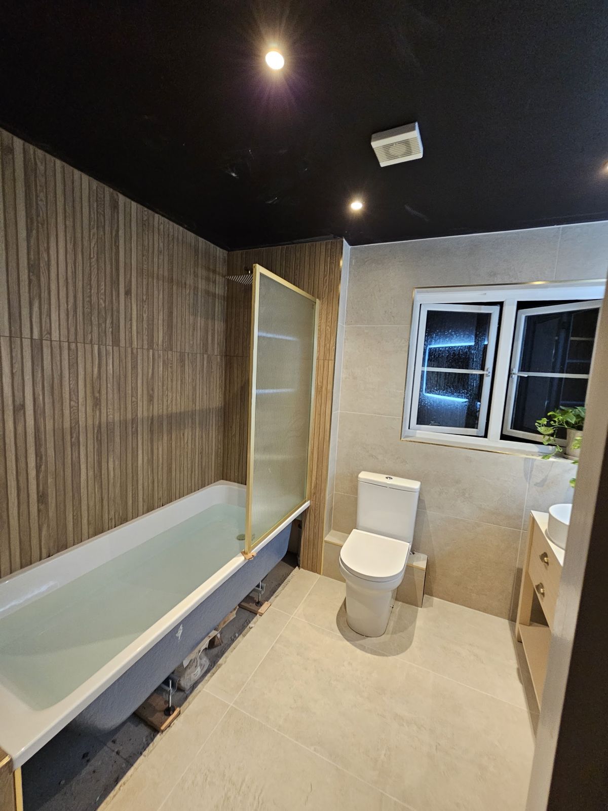 Finished bathroom with a bath, glass screen, wood slat wall panel and black ceiling
