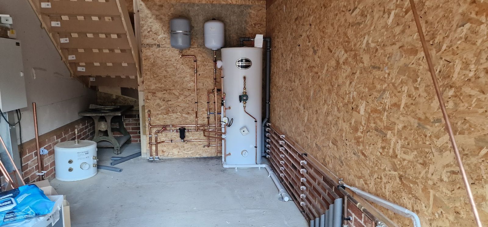 Outbuilding with a hot water cylinder and new pipework on wooden boards