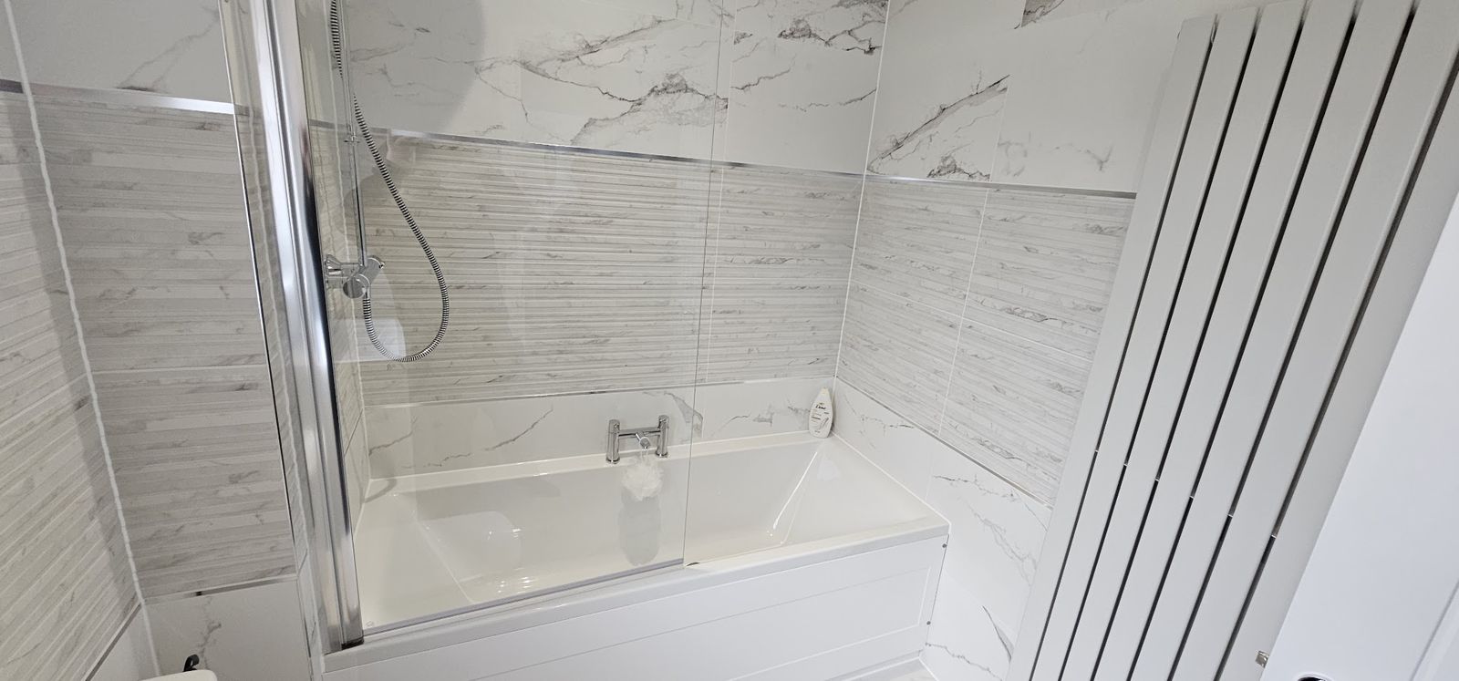 Marble-effect bathroom with a bath, shower screen and vertical radiator